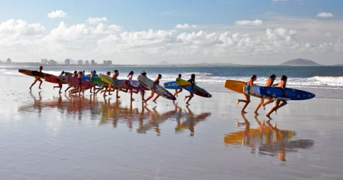 Group of surfers carrying surfboards down towards the sea